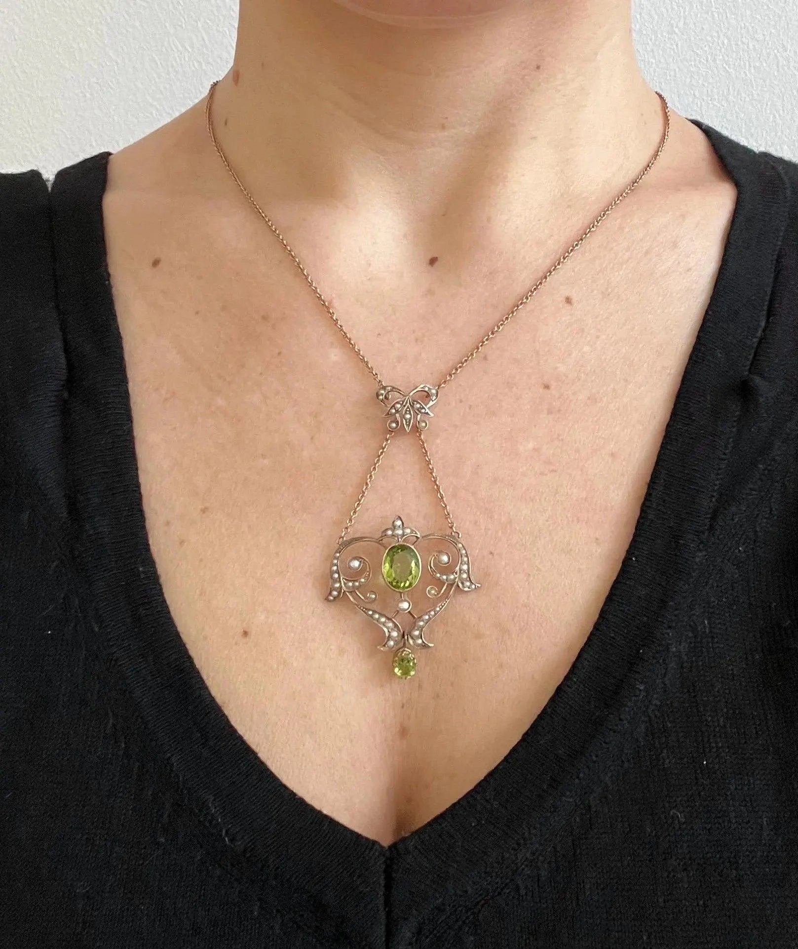 A yellow gold peridot and seed pearl pendant necklace, modelled by a woman wearing a black top