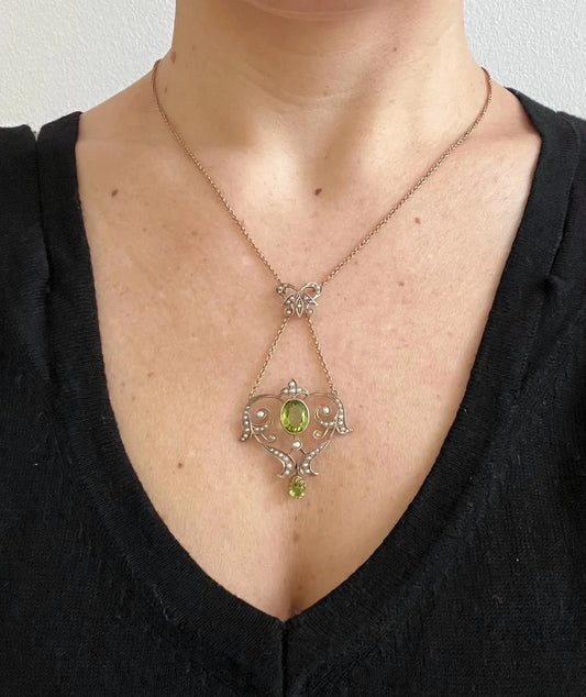 A yellow gold peridot and seed pearl pendant necklace, modelled by a woman wearing a black top