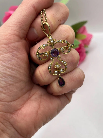A yellow gold amethyst and seed pearl pendant/brooch, with a gold chain, held in a hand