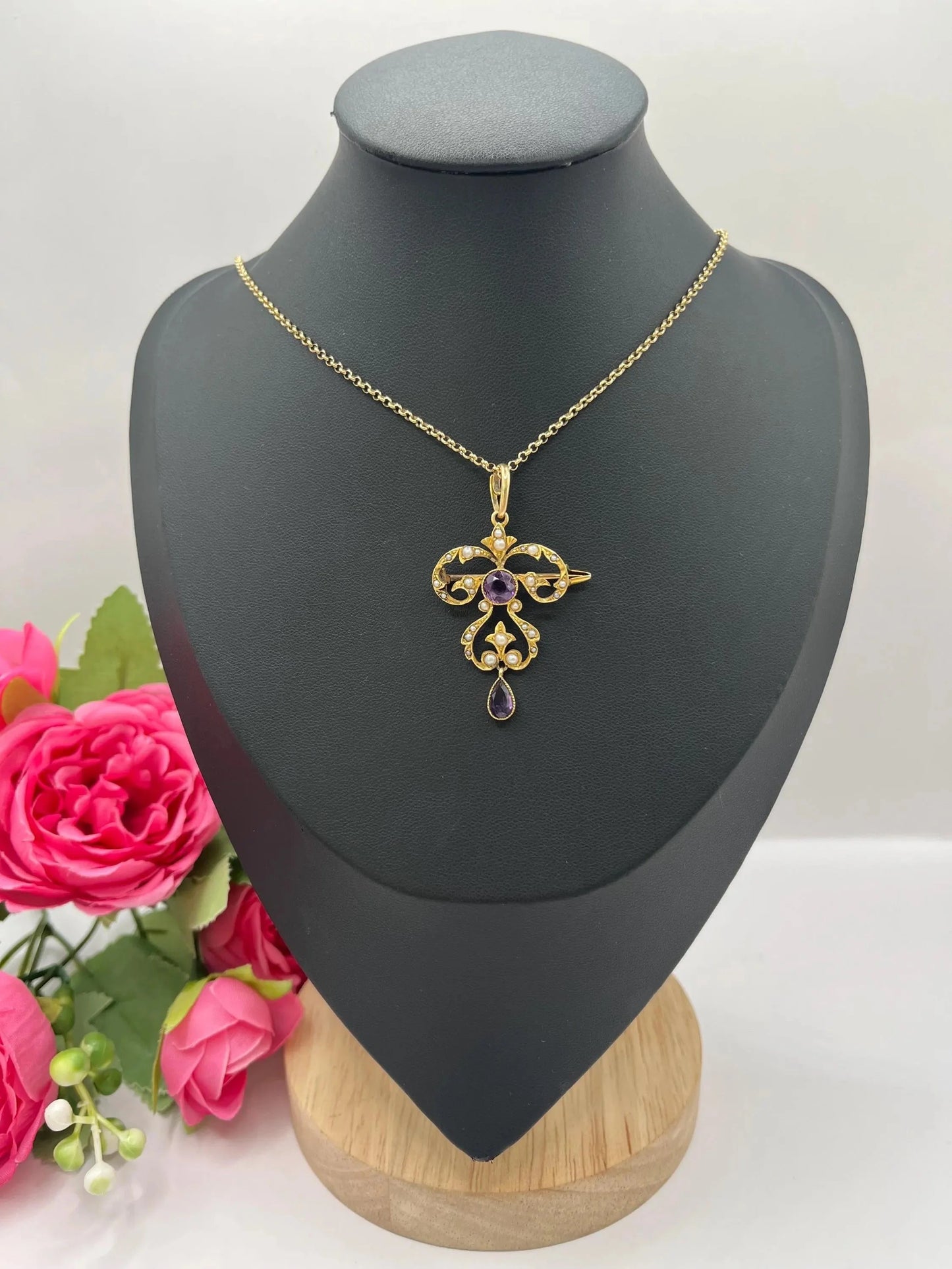 A yellow gold amethyst and seed pearl pendant/brooch, with a gold chain, on a black jewellery bust