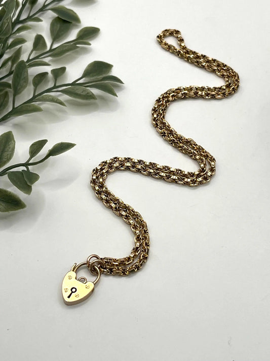 A yellow gold chain necklace with a heart shaped padlock clasp
