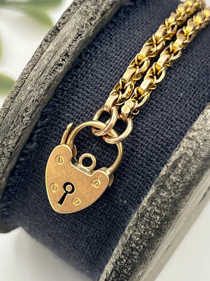A yellow gold chain necklace with a heart shaped padlock clasp