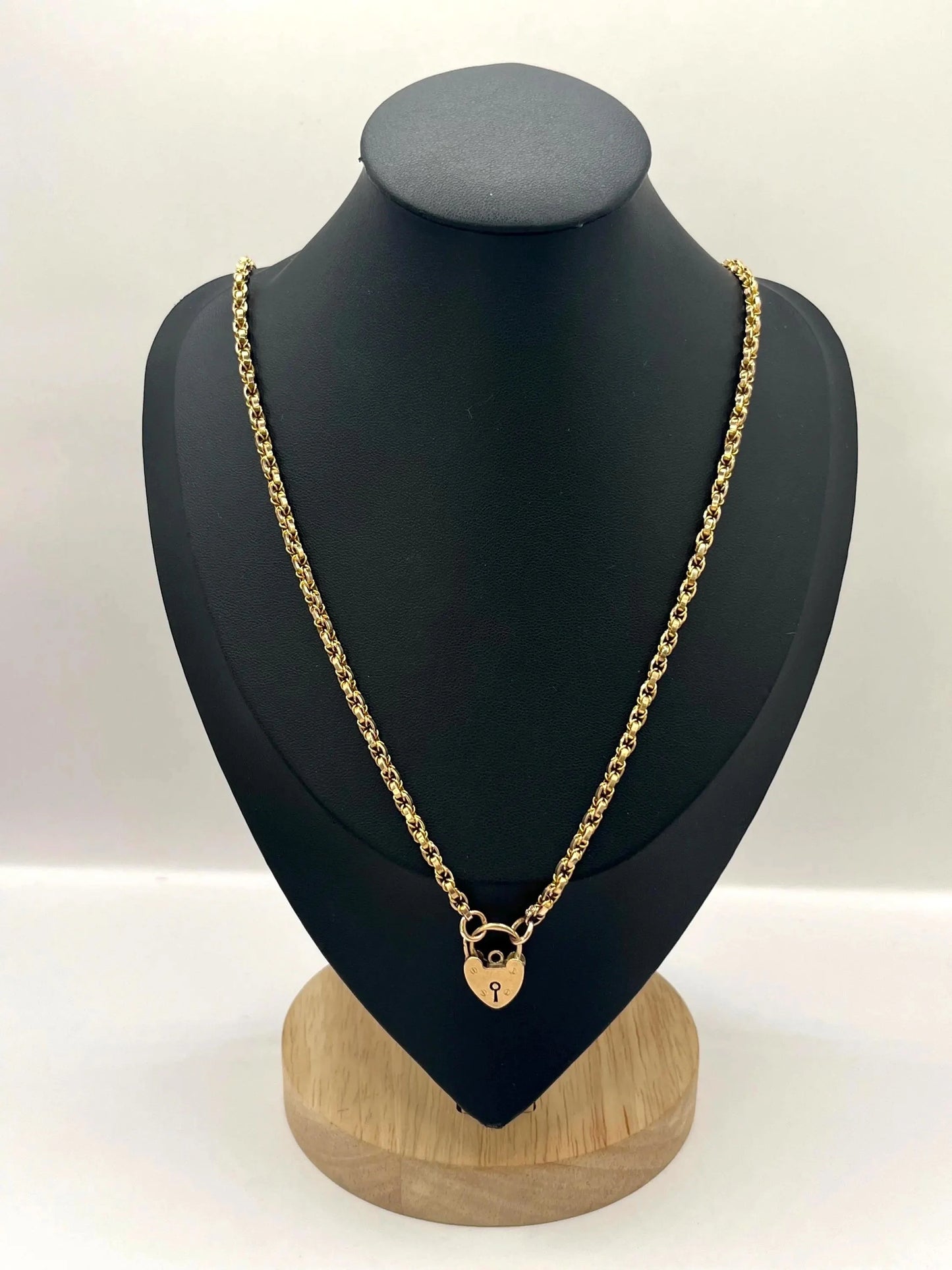 A yellow gold chain necklace with a heart shaped padlock clasp, on a black jewellery bust