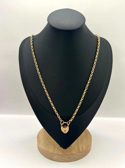 A yellow gold chain necklace with a heart shaped padlock clasp, on a black jewellery bust