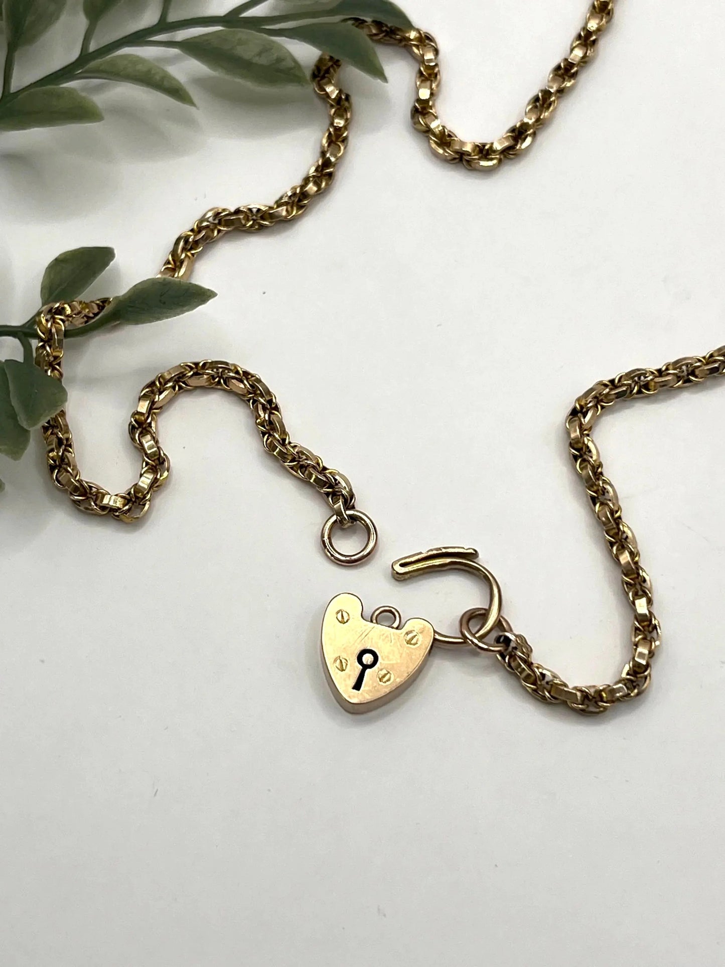 A yellow gold chain necklace with a heart shaped padlock clasp