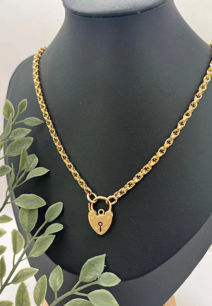 A yellow gold chain necklace with a heart shaped padlock clasp, on a black jewellery bust