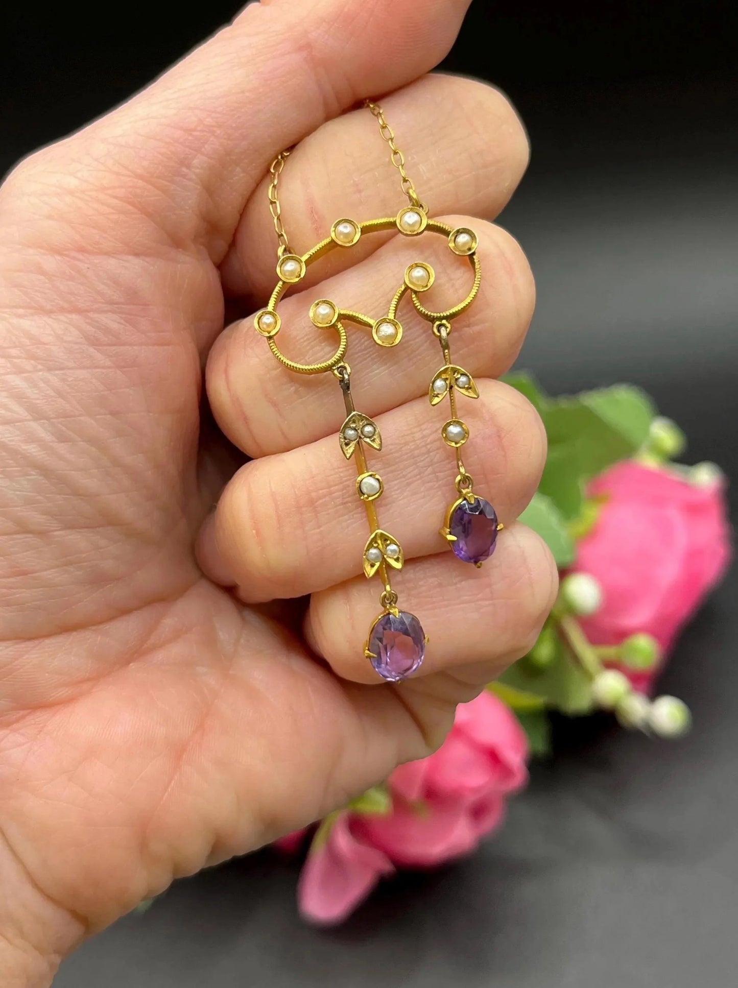 An amethyst and seed pearl drop pendant necklace in yellow gold, held in a hand