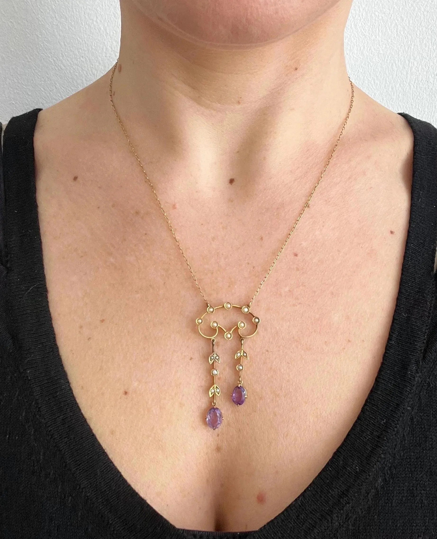 An amethyst and seed pearl drop pendant necklace in yellow gold, modelled by a woman wearing a black top