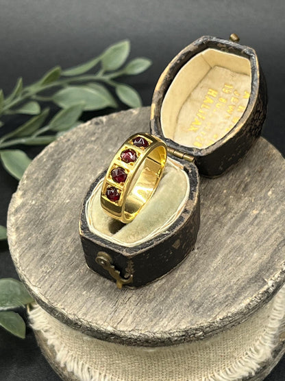 A yellow gold four stone garnet band ring, in an antique ring box