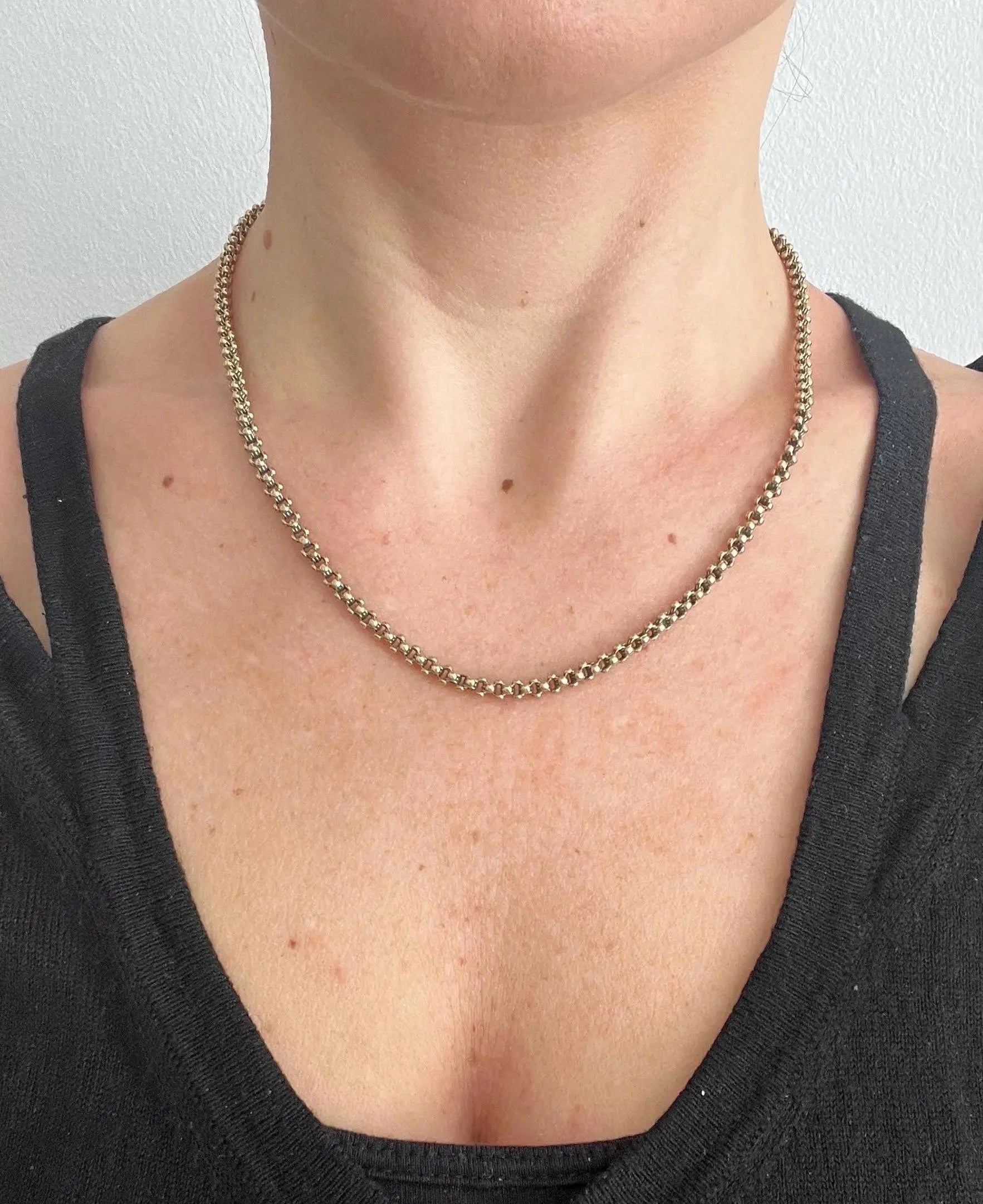 A yellow gold belcher link chain necklace, modelled by a woman wearing a black top