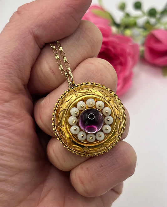A round etruscan style pendant with a cabochon amethyst and carved coral in yellow gold, with a gold chain, held in a hand