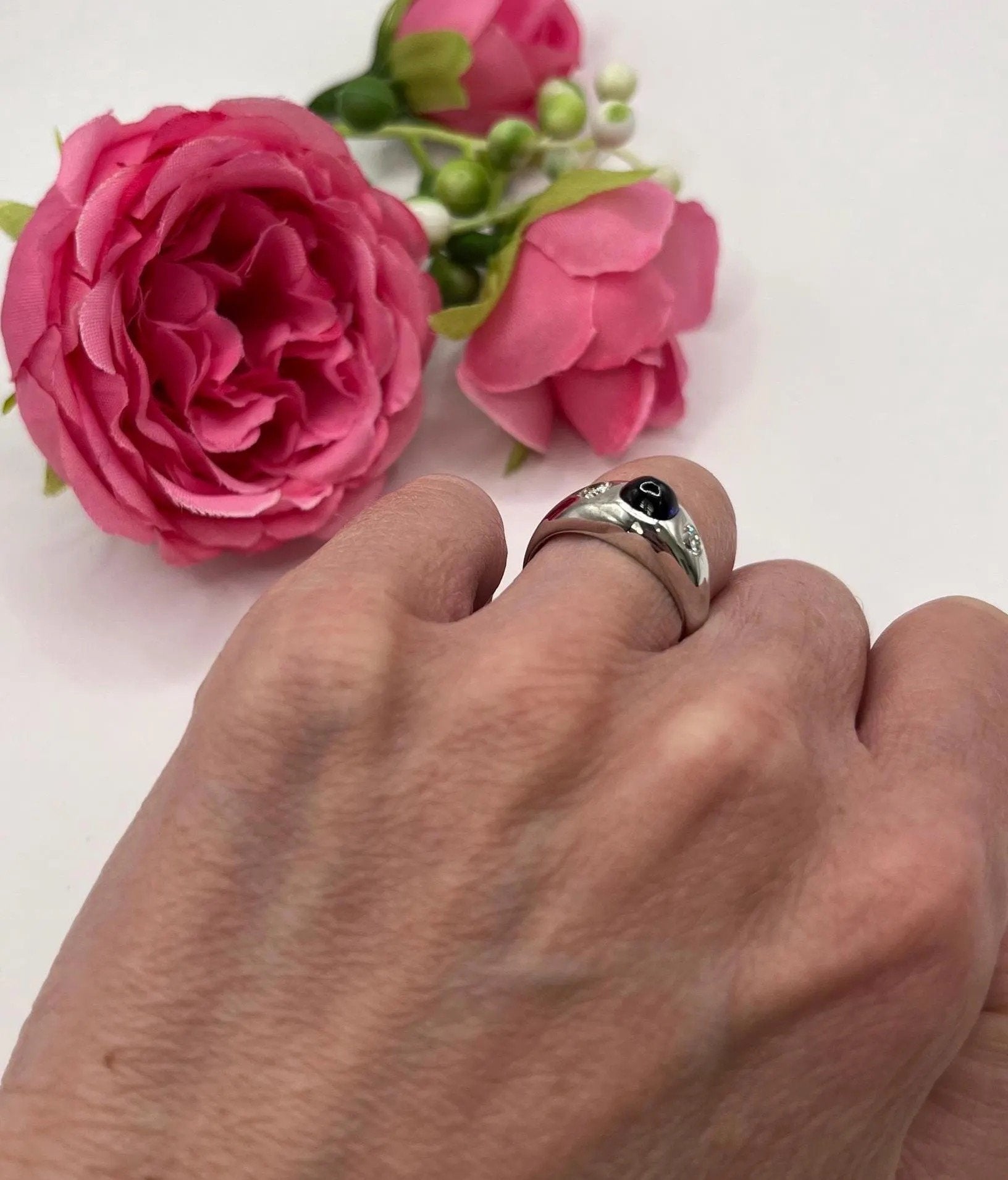 A cabochon sapphire and round diamond three stone band ring in white gold, modelled on a hand