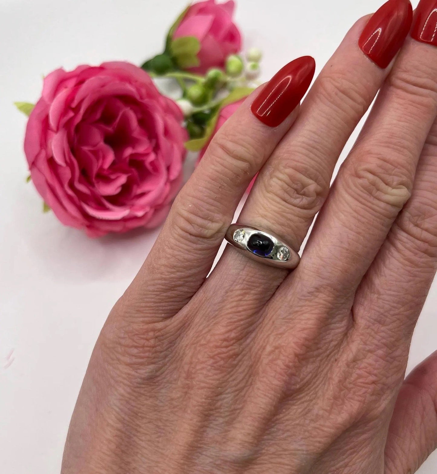 A cabochon sapphire and round diamond three stone band ring in white gold, modelled on a hand