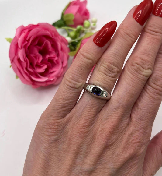 A cabochon sapphire and round diamond three stone band ring in white gold, modelled on a hand