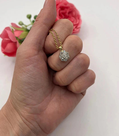 A diamond cluster pendant in yellow and white gold with a yellow gold chain, held in a hand