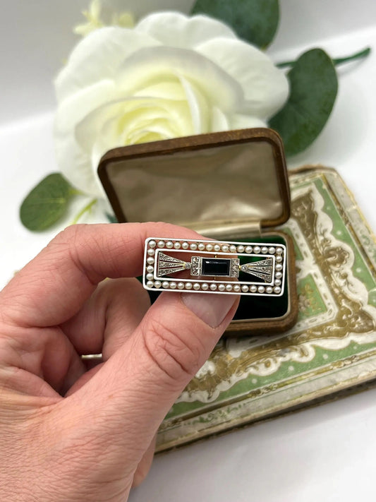 A rectangular brooch with sapphire, pearls and diamonds in gold and platinum, held in a hand