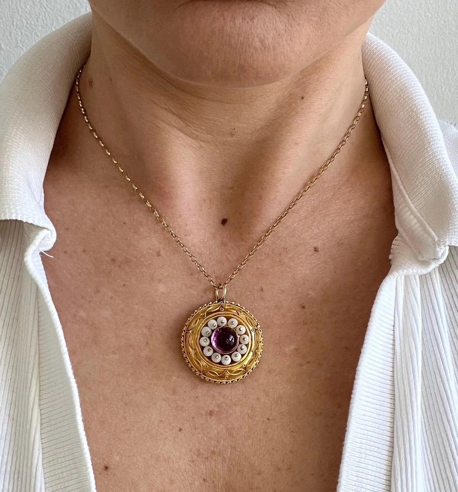 A round etruscan style pendant with a cabochon amethyst and carved coral in yellow gold, modelled with a gold chain