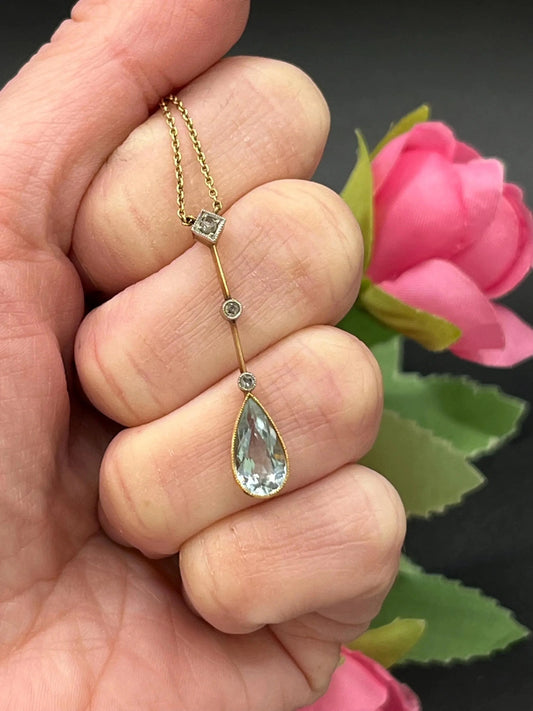 A pear shaped aquamarine and diamond drop pendant necklace in yellow gold, held in a hand