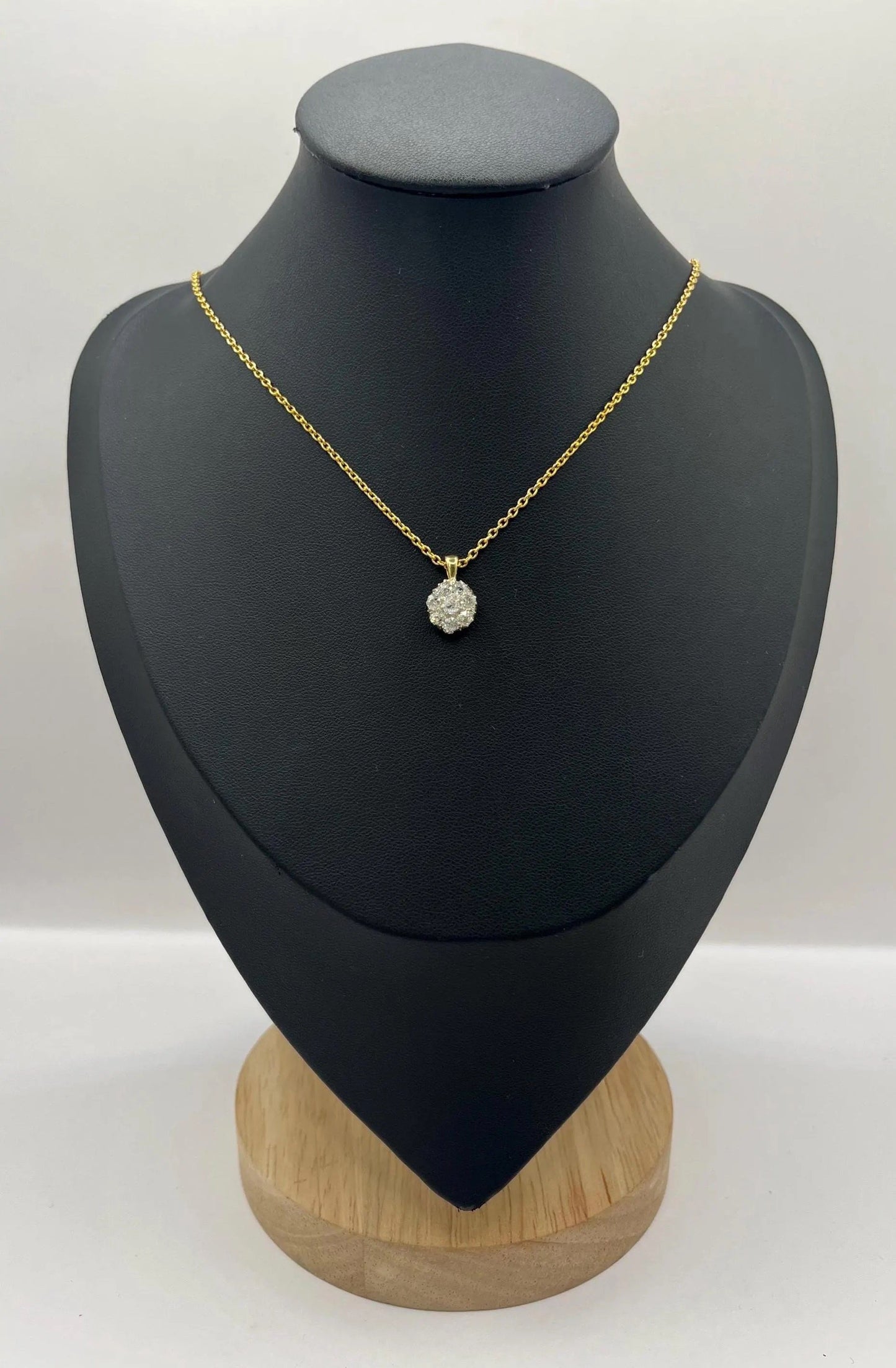 A diamond cluster pendant in yellow and white gold with a yellow gold chain, on a black jewellery bust