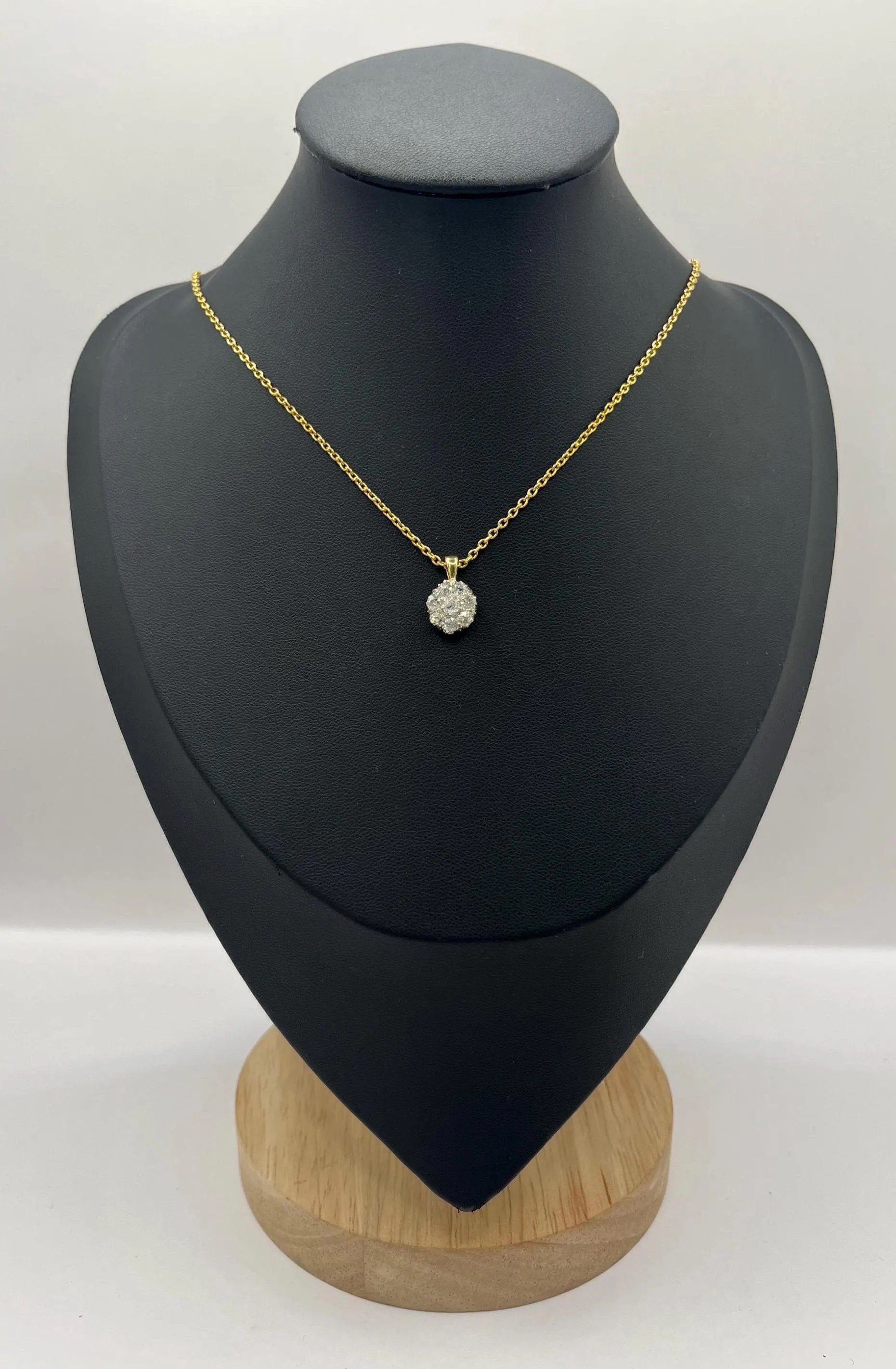 A diamond cluster pendant in yellow and white gold with a yellow gold chain, on a black jewellery bust