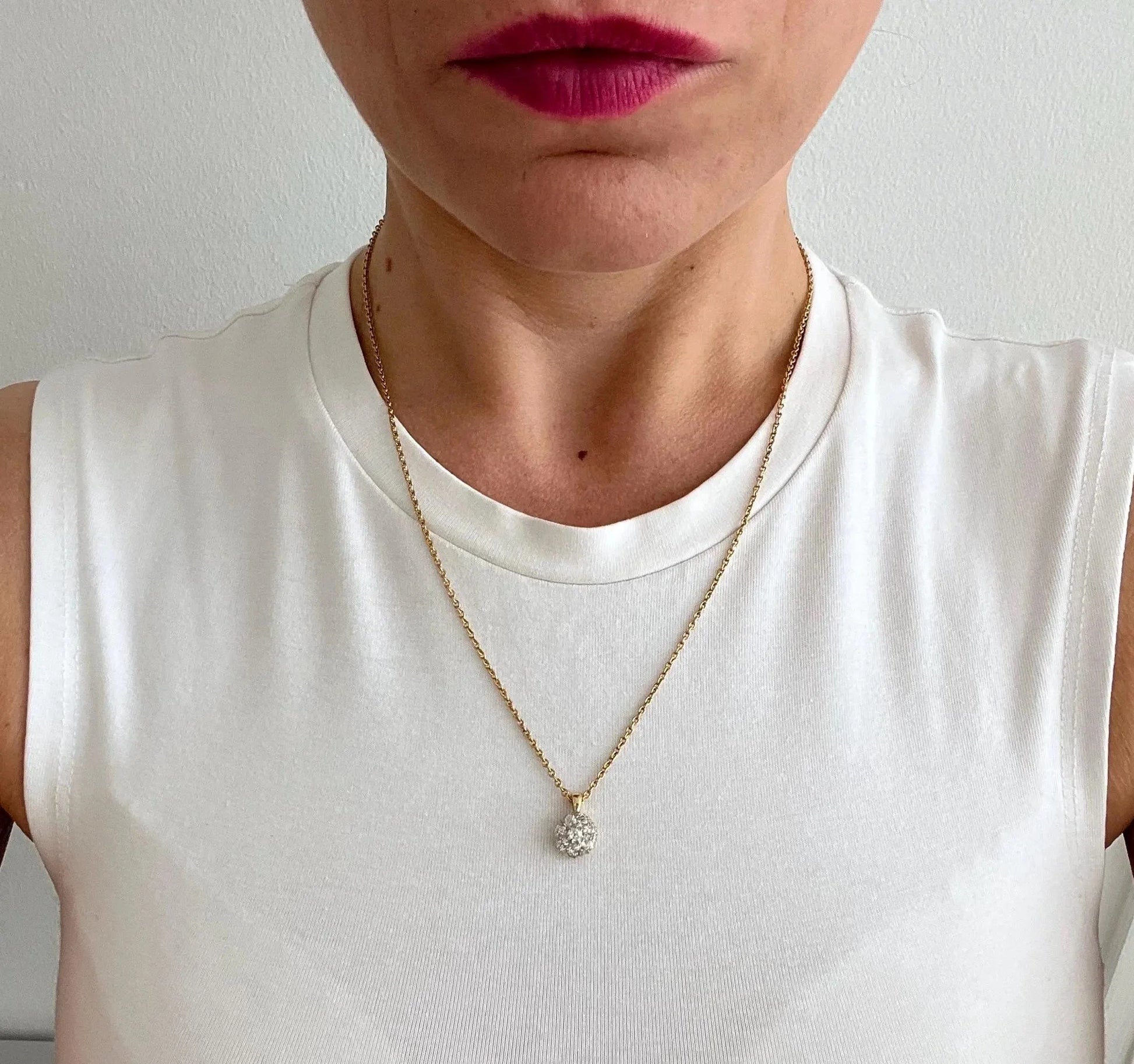 A diamond cluster pendant in yellow and white gold with a yellow gold chain, modelled by a woman wearing a white top