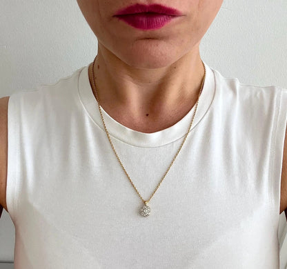 A diamond cluster pendant in yellow and white gold with a yellow gold chain, modelled by a woman wearing a white top
