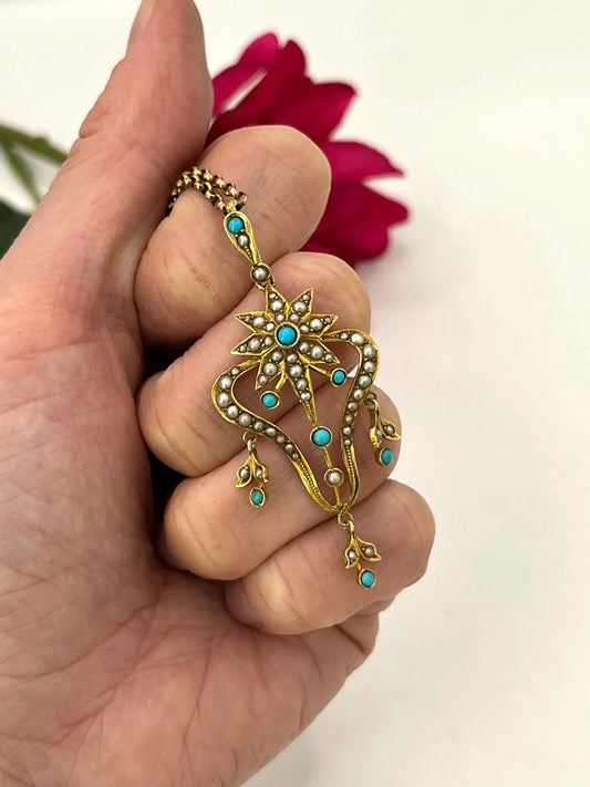 A yellow gold turquoise and pearl decorative openwork drop pendant, with a gold chain, held in a hand