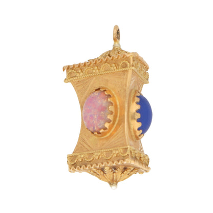 A yellow gold Chinese lantern charm with a pink and blue stone on a white background