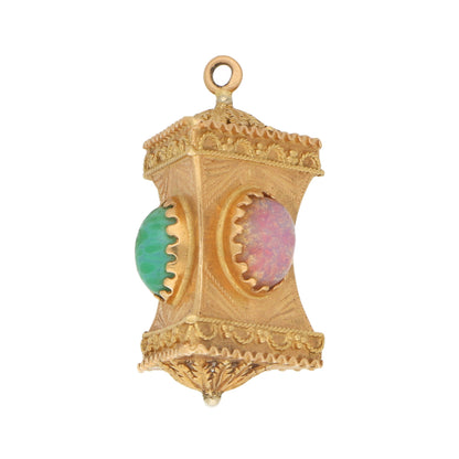 A yellow gold Chinese lantern charm with a pink and green stone on a white background
