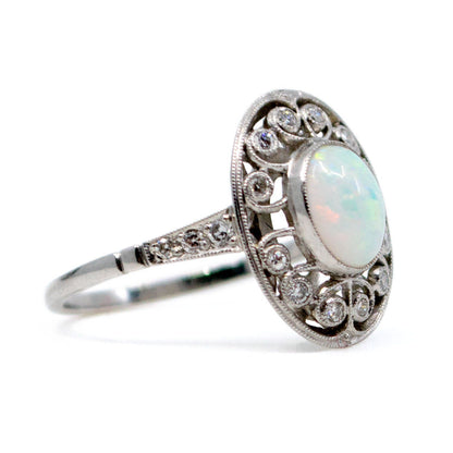 An oval shaped openwork ring with an opal centre and diamonds in swirl settings, in platinum