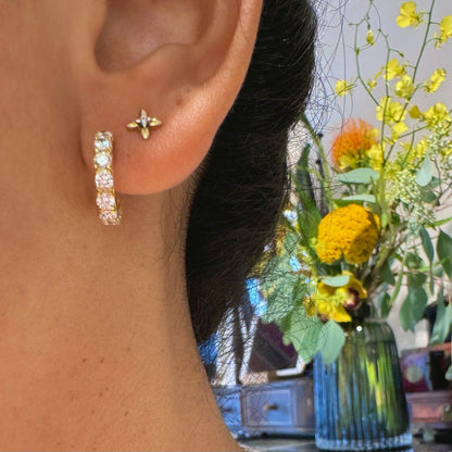 A diamond half hoop earring in yellow gold, and a small diamond stud, modelled in an ear