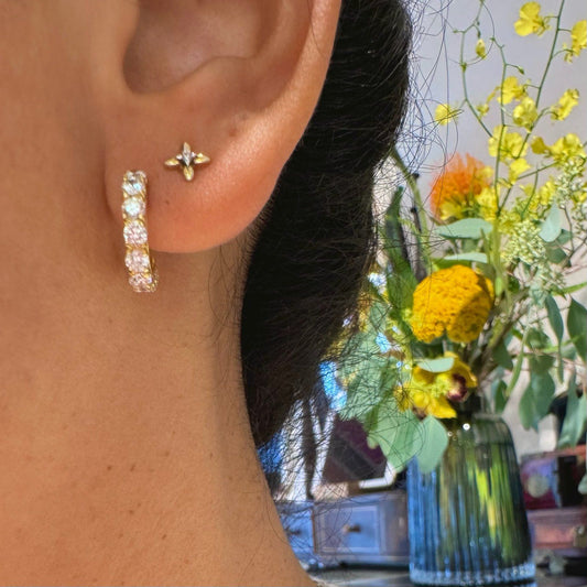 A diamond half hoop earring in yellow gold, and a small diamond stud, modelled in an ear