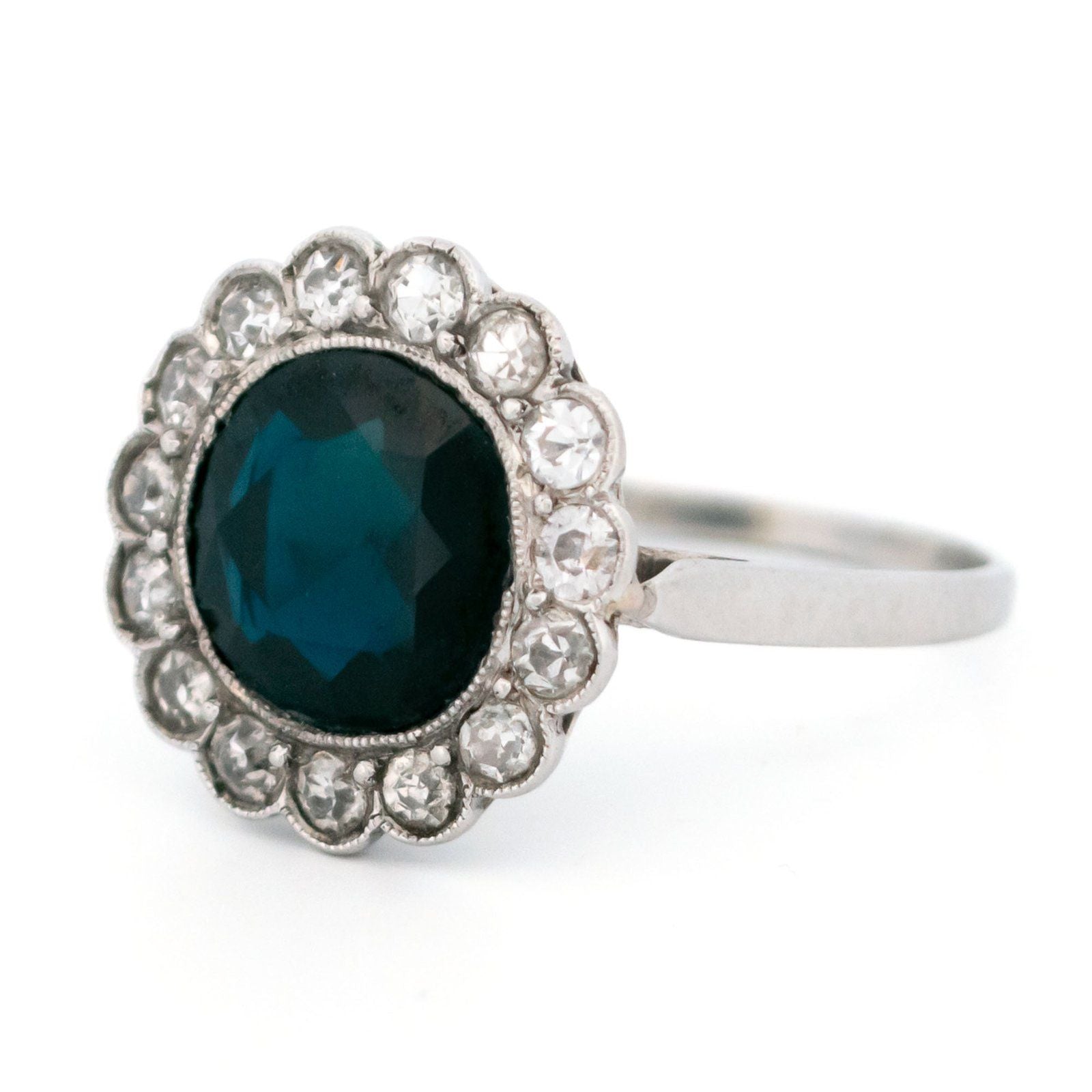 A flower shaped cluster ring set with a central sapphire surrounded by a halo of round diamonds, in platinum