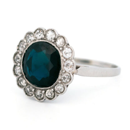 A flower shaped cluster ring set with a central sapphire surrounded by a halo of round diamonds, in platinum