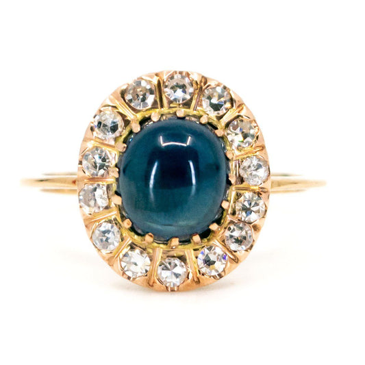 An oval cluster ring with a cabochon sapphire and diamond surround, in yellow gold