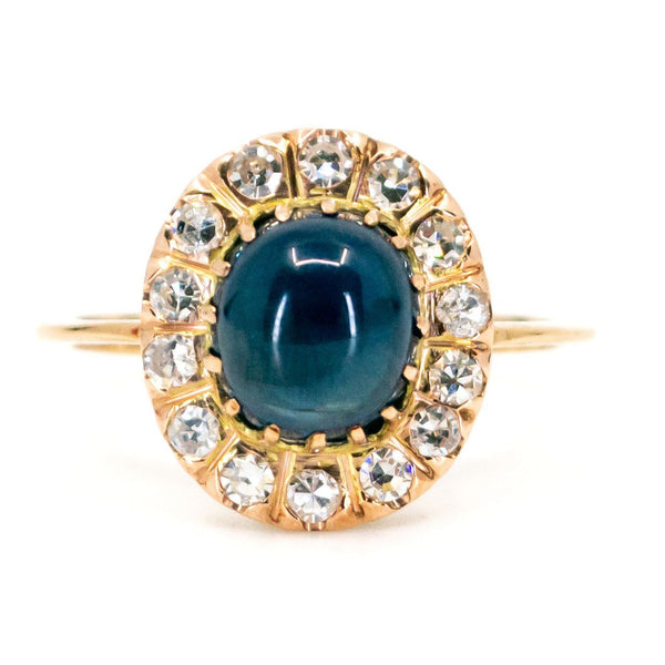 An oval cluster ring with a cabochon sapphire and diamond surround, in yellow gold