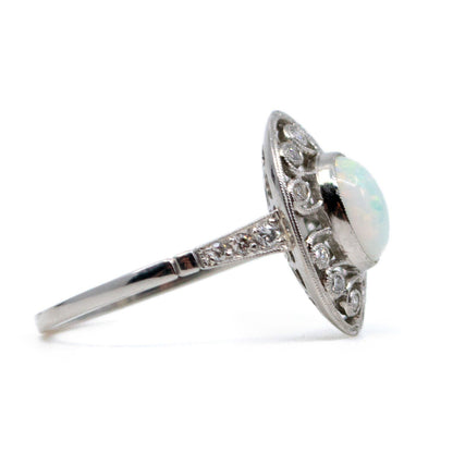 An oval shaped openwork ring with an opal centre and diamonds in swirl settings, in platinum