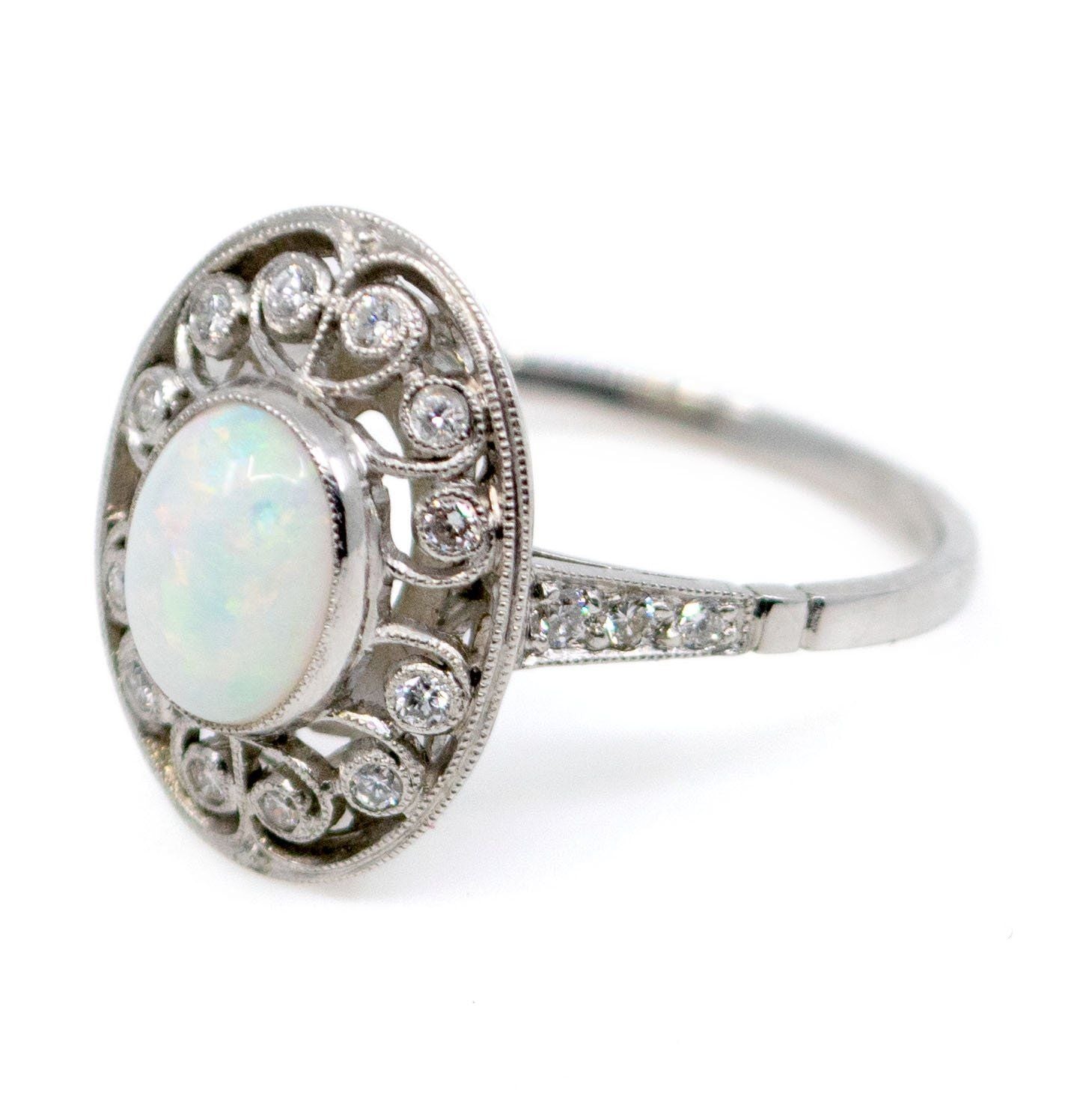 An oval shaped openwork ring with an opal centre and diamonds in swirl settings, in platinum