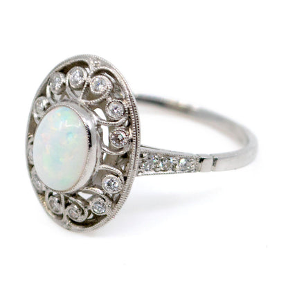 An oval shaped openwork ring with an opal centre and diamonds in swirl settings, in platinum