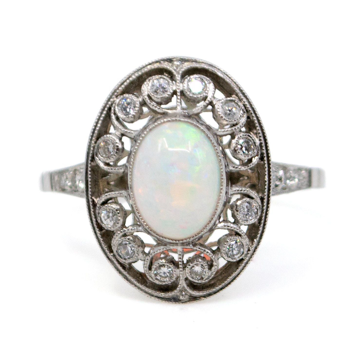An oval shaped openwork ring with an opal centre and diamonds in swirl settings, in platinum