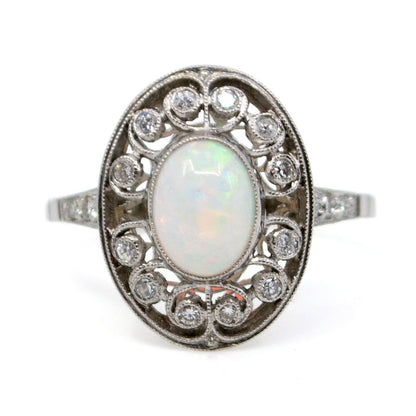 An oval shaped openwork ring with an opal centre and diamonds in swirl settings, in platinum