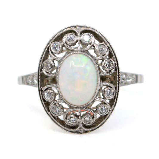 An oval shaped openwork ring with an opal centre and diamonds in swirl settings, in platinum