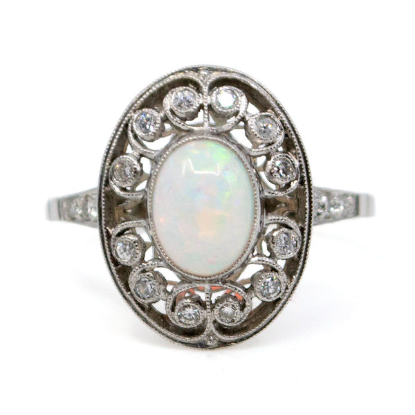 An oval shaped openwork ring with an opal centre and diamonds in swirl settings, in platinum