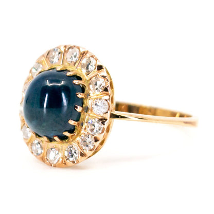 An oval cluster ring with a cabochon sapphire and diamond surround, in yellow gold