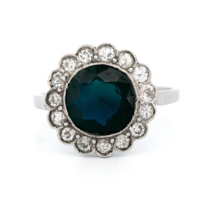 A flower shaped cluster ring set with a central sapphire surrounded by a halo of round diamonds, in platinum