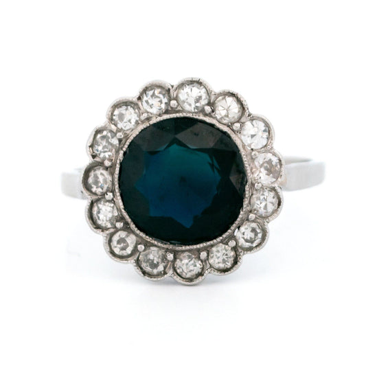 A flower shaped cluster ring set with a central sapphire surrounded by a halo of round diamonds, in platinum