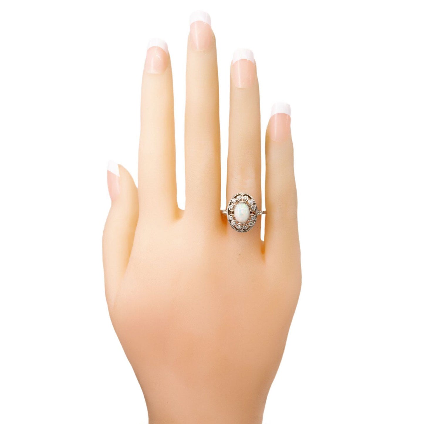 An oval shaped openwork ring with an opal centre and diamonds in swirl settings, in platinum, modelled on a plastic hand
