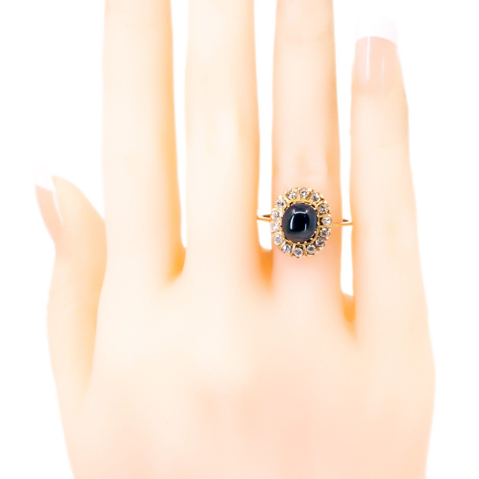 An oval cluster ring with a cabochon sapphire and diamond surround, in yellow gold, modelled on a plastic hand