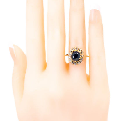An oval cluster ring with a cabochon sapphire and diamond surround, in yellow gold, modelled on a plastic hand