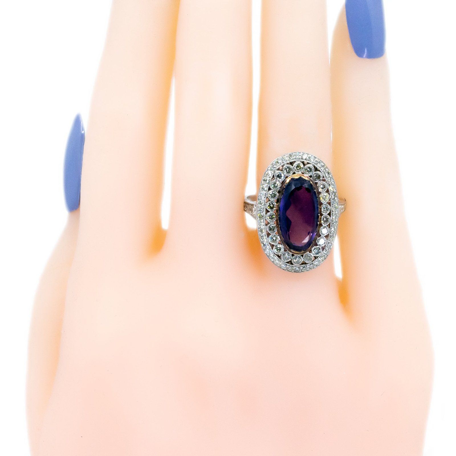 An oval shaped cluster ring with an amethyst centre and diamond surround, in platinum, modelled on a plastic hand